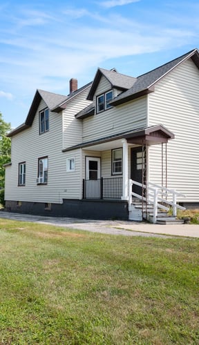 Two-story white Manistee home with front porch and green lawn on a summer day