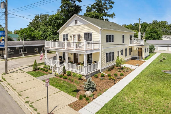Dala House in Onekama, Michigan: two-story cream building with double porches and American flag, aerial view on a sunny summer day.