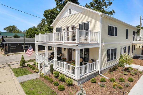 White two-story house with wraparound porches and white railings on a residential street