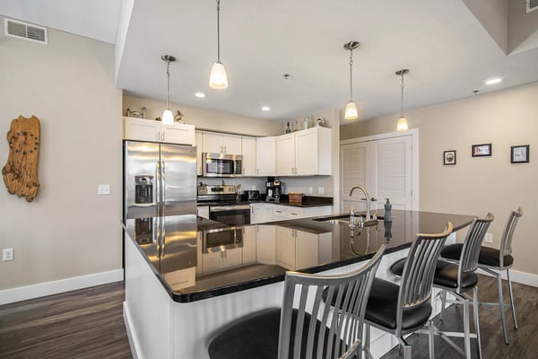 Condo kitchen with white cabinetry, dark granite island with bar seating, stainless steel appliances, and pendant lighting.