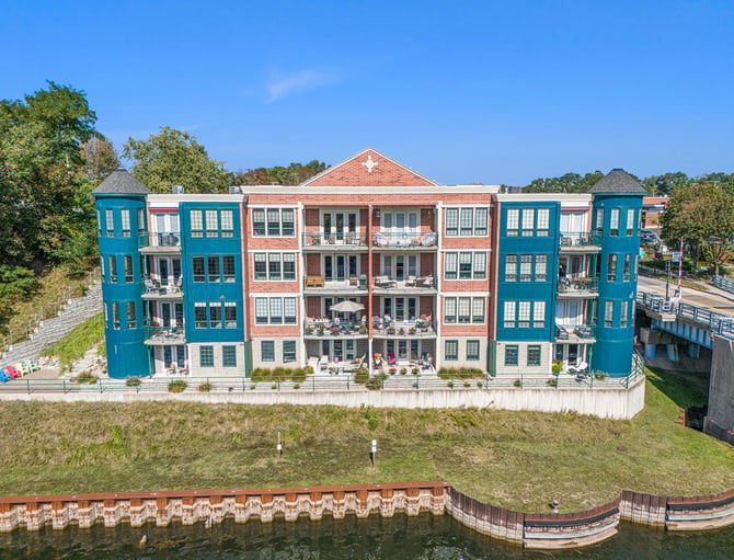 Waterfront apartment building with turquoise and brick facades, multiple balconies, and manicured grounds along a canal.